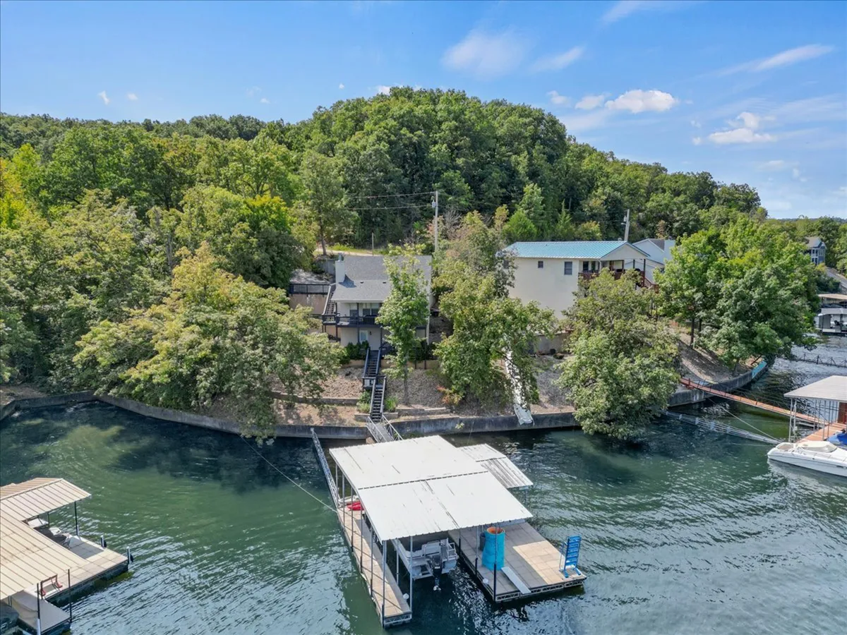 This image shows a serene waterfront scene featuring a private dock extending into the lake, surrounded by trees and neighboring homes. The tranquil water invites boating, swimming, and relaxing by the shore, while the dock provides a perfect spot to tie up a boat after a day of exploring.