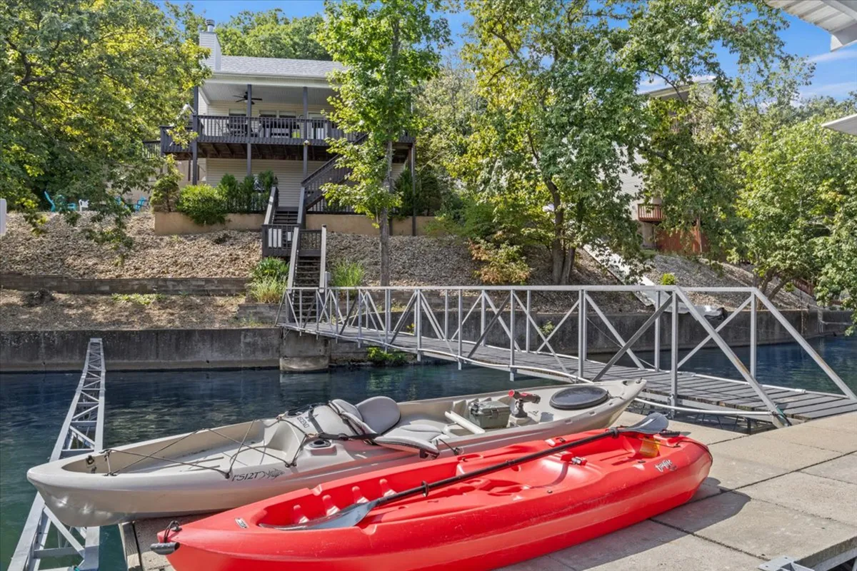 The image showcases the exterior of a lakefront single-family house nestled among lush greenery, with kayaks lined up on a private pier extending over deep, calm waters. A staircase leads from the house down to the water, inviting exploration and outdoor activities like kayaking, fishing, and relaxing by the lake. The overall scene exudes a sense of leisure, adventure, and connection with nature.