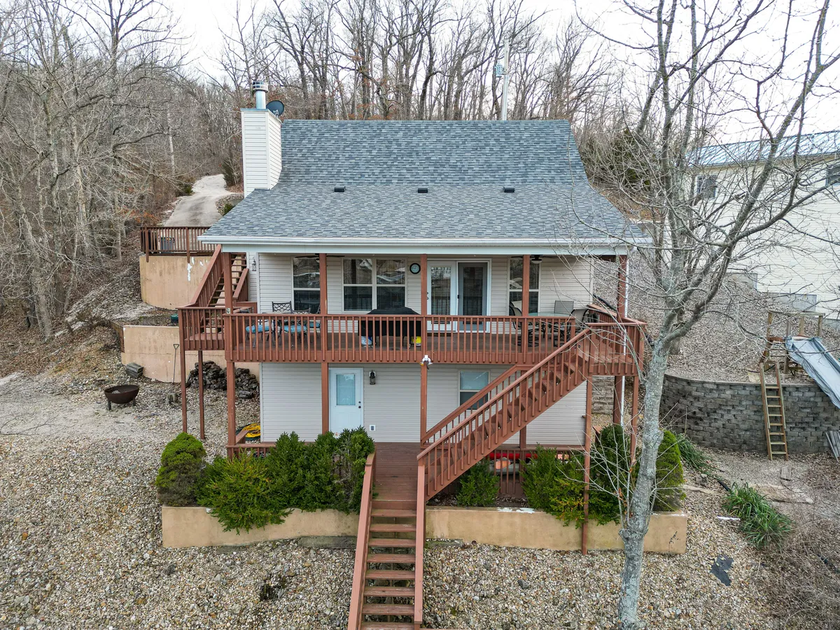 An exterior view of the house showing the structure itself, a spacious deck, surrounding trees, and a private driveway. This scene evokes a sense of seclusion, exclusivity, and tranquility, with the home's setting nestled in nature.