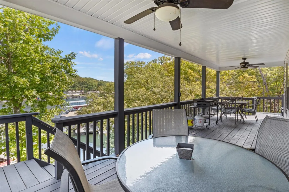 This image features an outdoor dining table situated on a deck with a clear view of the lake, surrounded by lush trees. The serene setting is perfect for relaxing meals outdoors, with room for a group to gather and enjoy the natural scenery. The angle shows both the dining setup and the proximity to the water, encapsulating the al fresco dining experience described in the section.