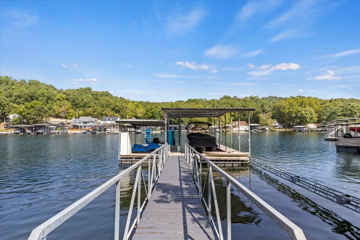 A serene waterfront scene with a dock extending over the glistening lake, surrounded by trees. Several boats are visible, emphasizing recreational boating and the peacefulness of lakeside living. The image captures the essence of lakefront access and the beauty of the secluded cove.