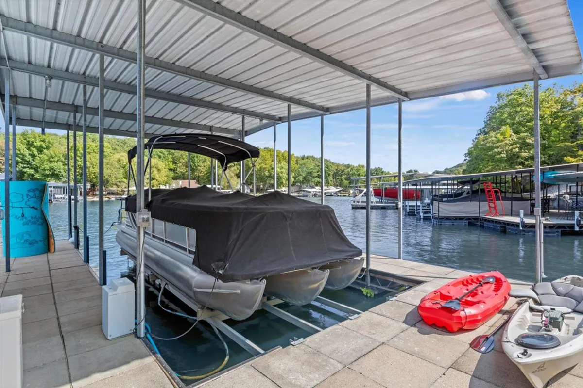 A tranquil lakeside scene featuring a pontoon boat docked beside a kayak on a private dock. The water is calm and inviting, surrounded by lush greenery. The image highlights both boating and kayaking opportunities, and the dock appears easily accessible for swimmers and those using watercraft.