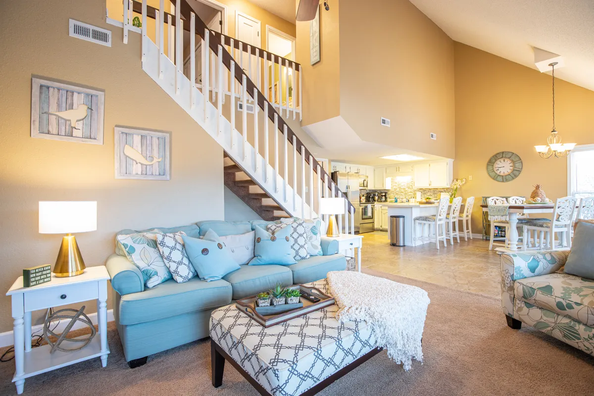 A cozy, inviting living area with a sofa, staircase, and view toward the adjoining dining space. Warm lighting and wall decor create a comfortable ambiance, making this an ideal spot for socializing, relaxing, or celebrating with family and friends.