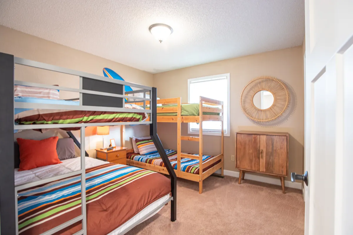 A cheerful bedroom with colorful bunk beds, a nightstand, a mirror, and vibrant bedding. The space is playful yet cozy, ideal for kids or friends sharing a room, and creates a sense of family bonding and fun sleepovers.