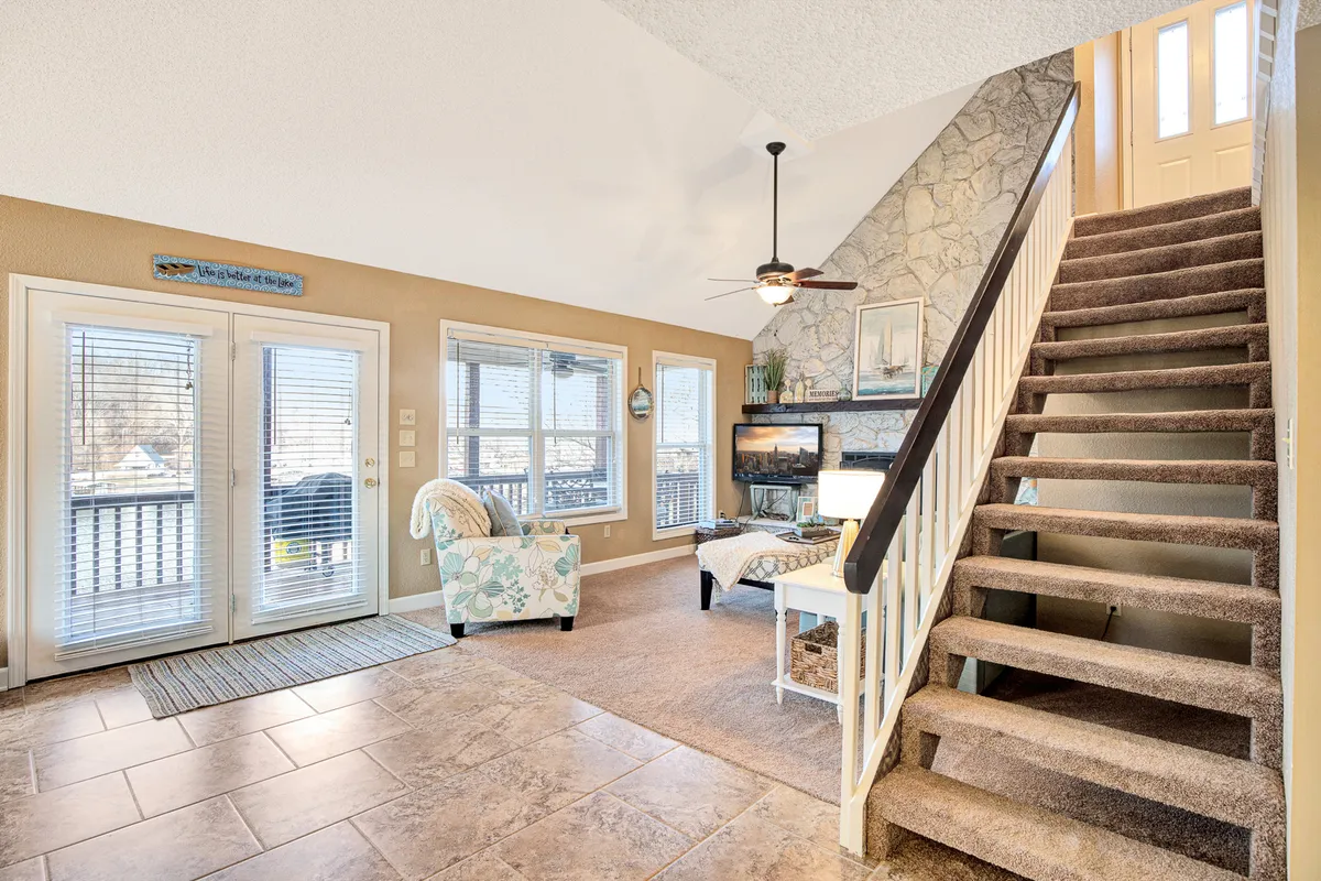 A welcoming entryway area featuring stairs leading to the upper level, a stone fireplace, large windows flooding the space with natural light, and a cozy seating area. The atmosphere is open and inviting, emphasizing the home's sense of comfort and security.